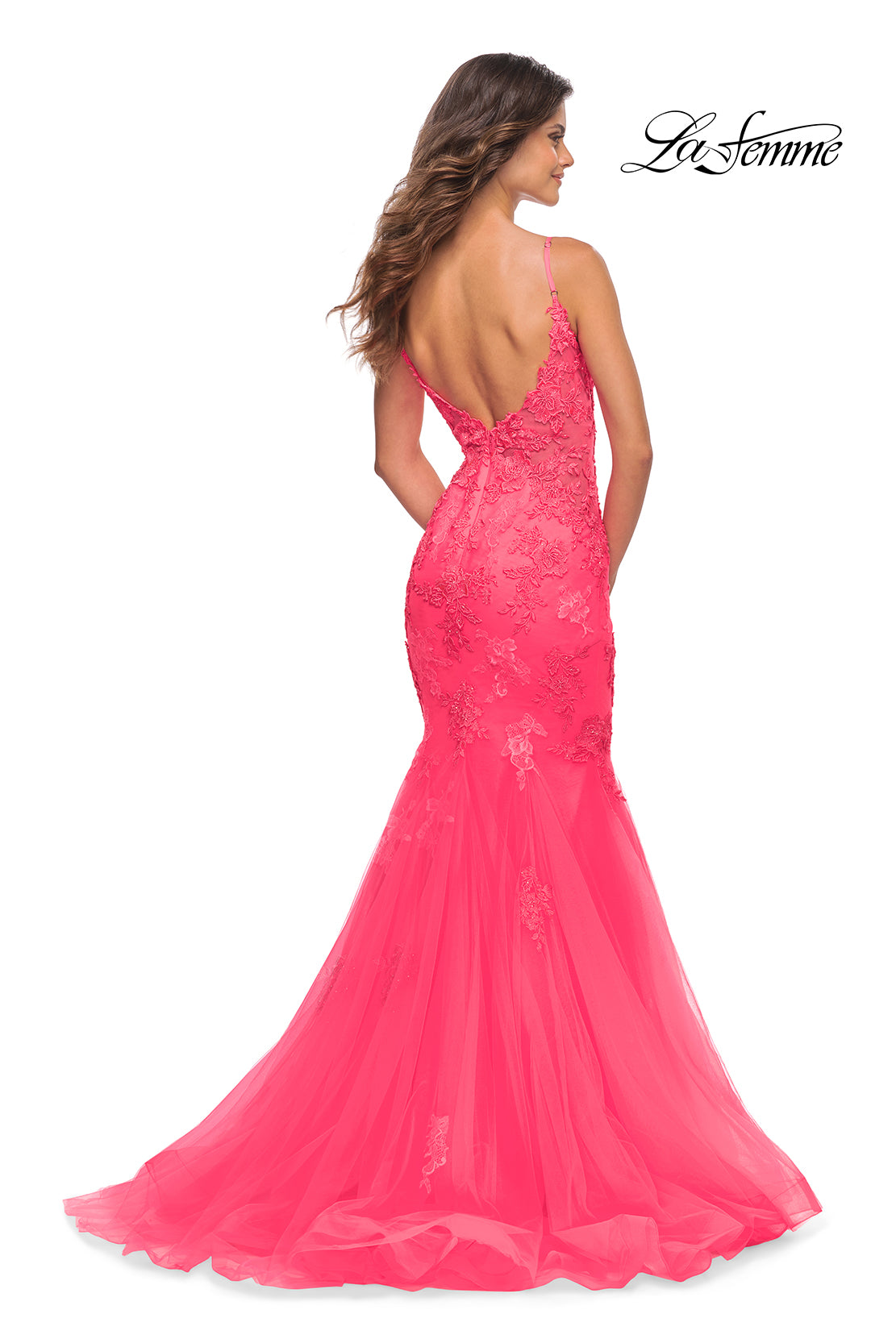 A woman in the La Femme Neon Pink Long Mermaid Prom Dress with lace details and a low back stands facing away, showcasing the floor-length, elegantly fitted style.